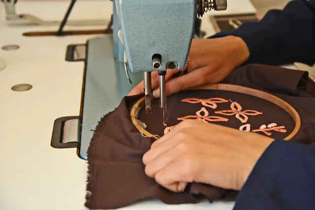 Close-up of hands embroidering fabric using a machine in a Fès artisan workshop. How NEC Shows Affect Midlands Promotional Products Orders